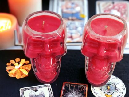Skull shaped glass candle jar on a table with playing cards surrounding.