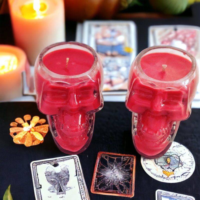 Skull shaped glass candle jar on a table with playing cards surrounding.