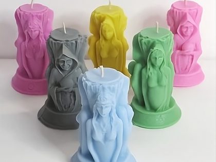 A collection of colorful Triple Goddess Candles in pink, grey, blue, green, and yellow, featuring the Maiden, Mother, and Crone figures.